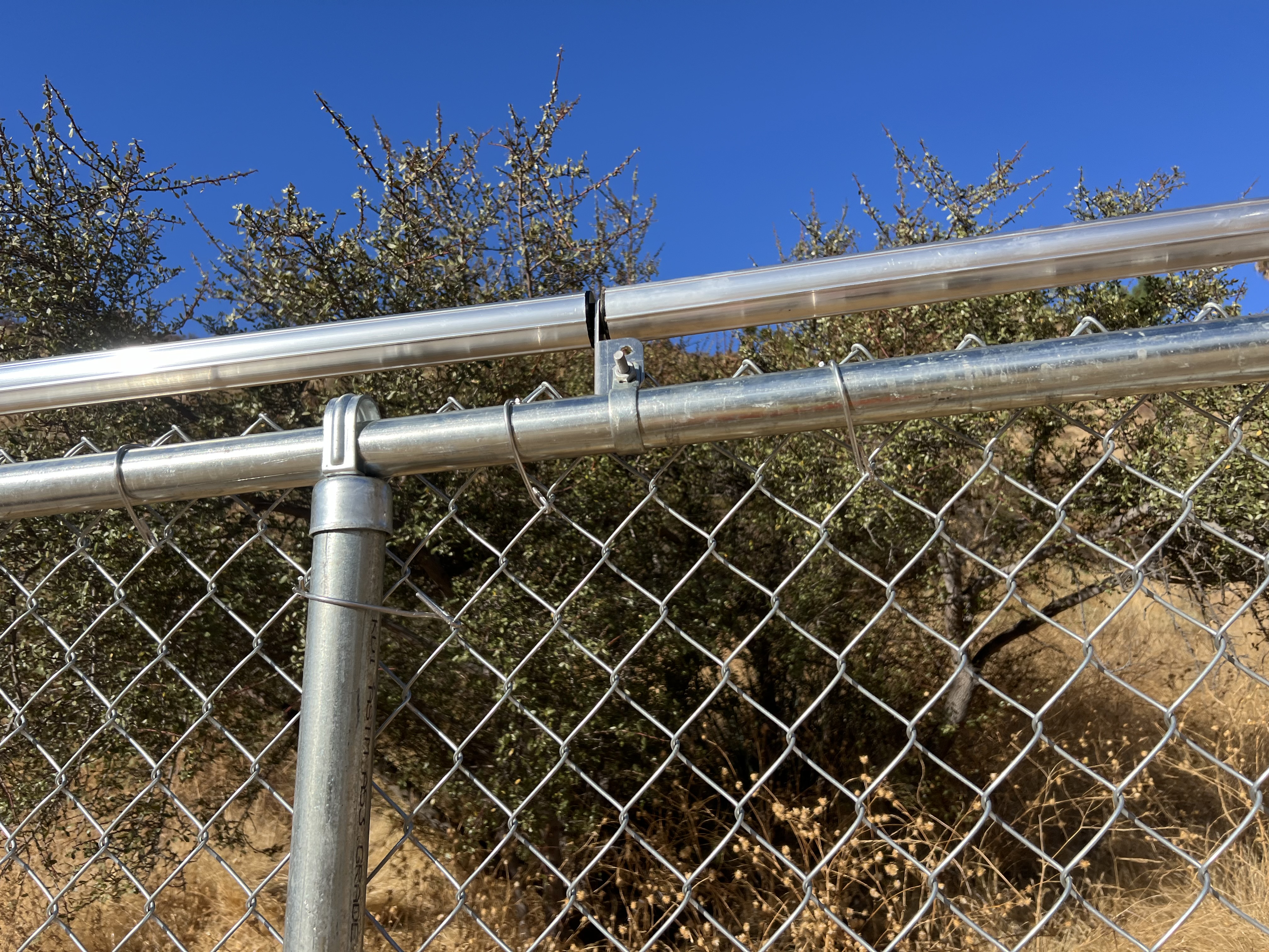 Galvanized chain-link fence close-up — top rail, tension bar, and mesh detail