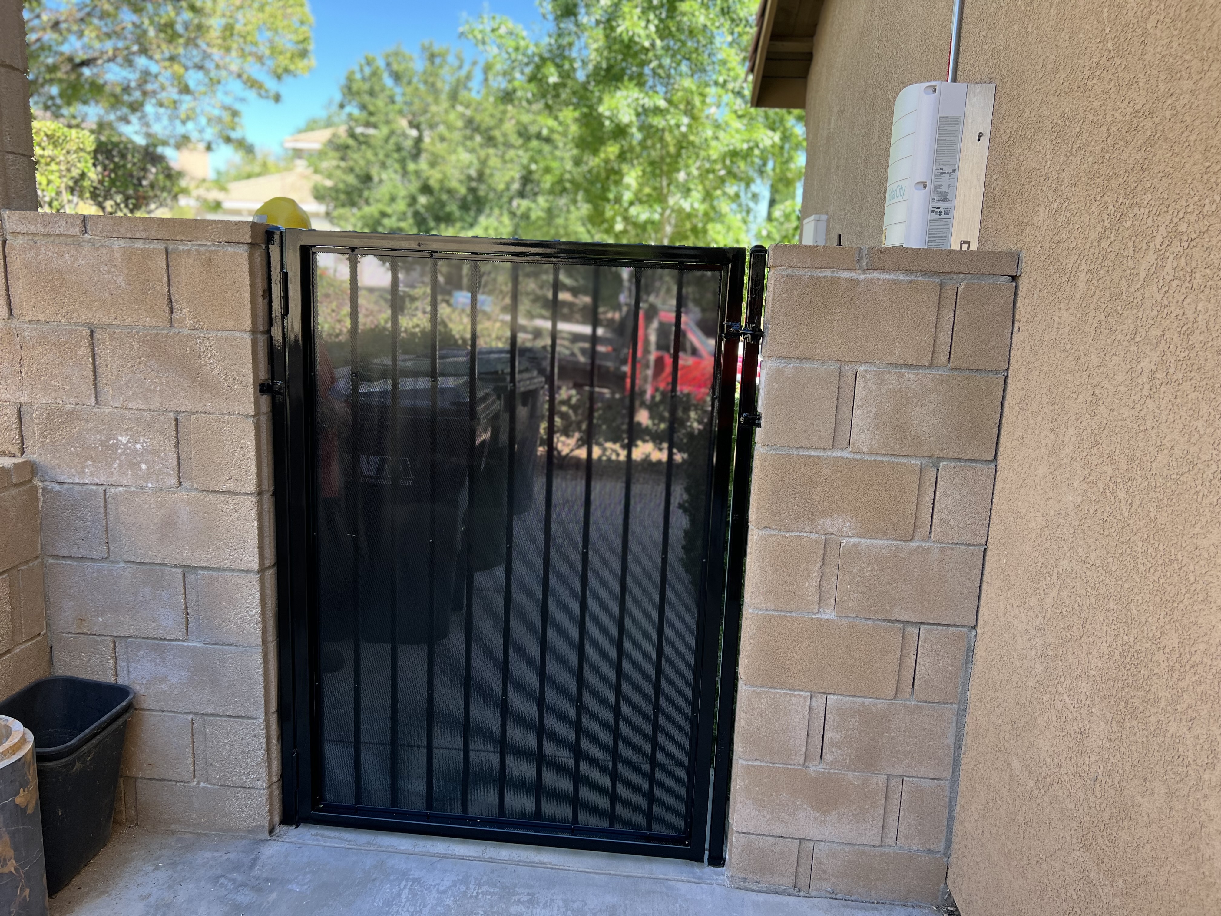 Black wrought iron pedestrian gate with mesh screen — open angle view