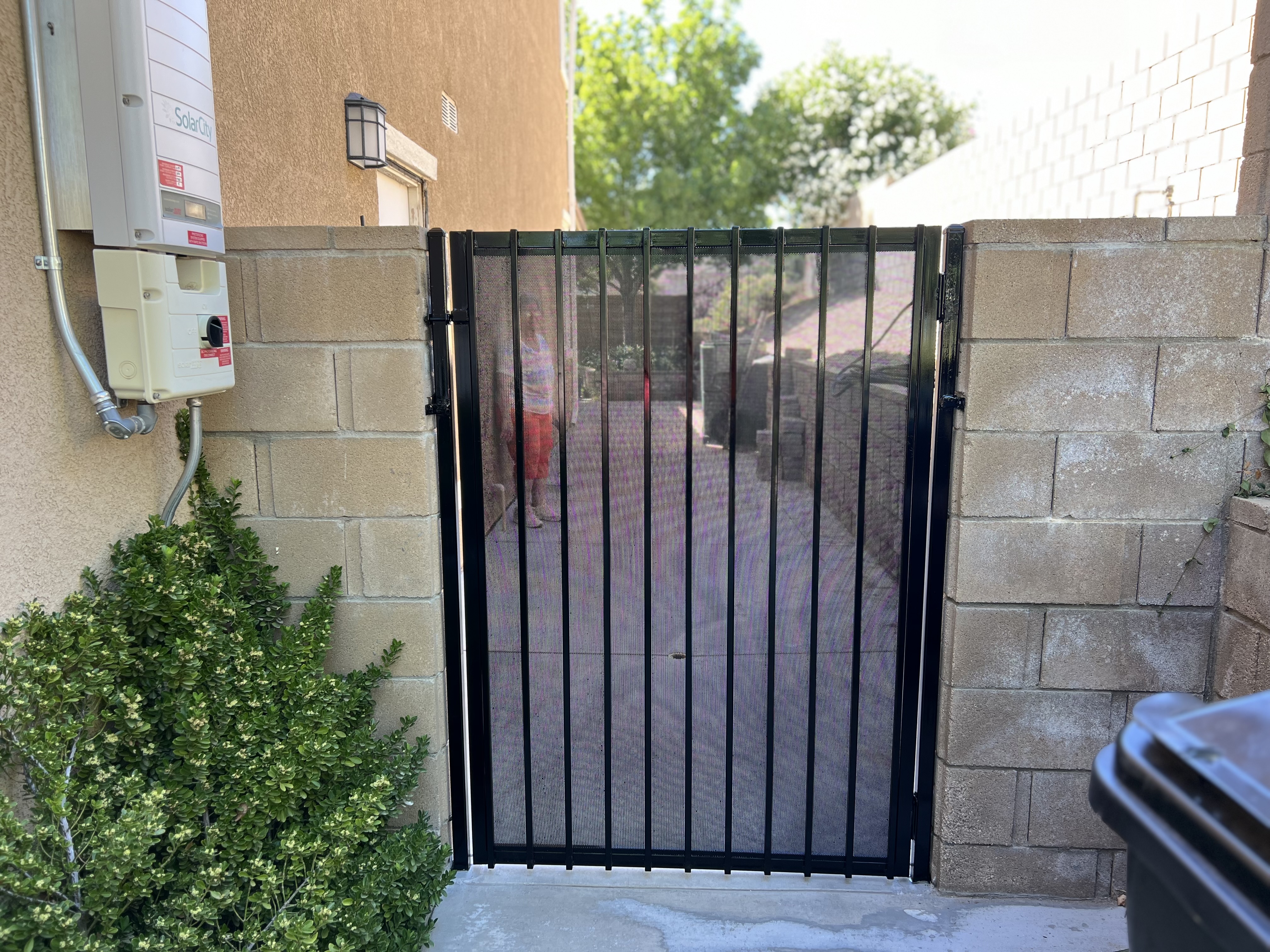Black wrought iron pedestrian gate with mesh screen between block walls — front view